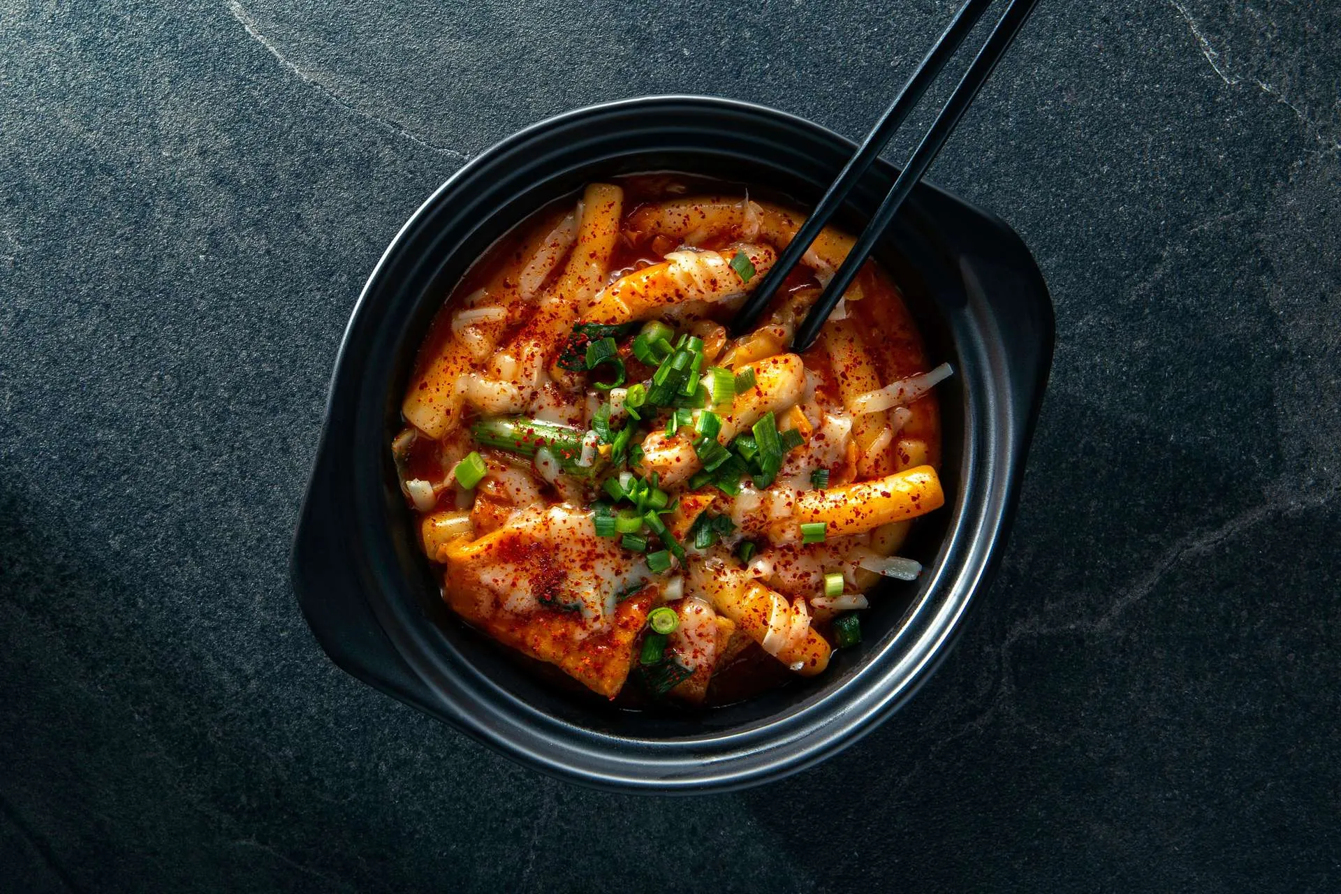 A bowl of Korean rice cakes with scallions and chili